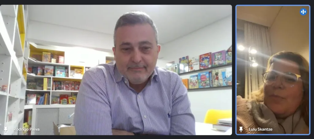 Captura de tela do Café com Aner sobre licenciamento mostra Rodrigo Paiva, homem branco de cabelos grisalhos em ambiente de escritório vestindo blusa de manga comprida e gola divide a tela com Lulu Skantze, mulher branca de óculos e cabelos castanhos claros