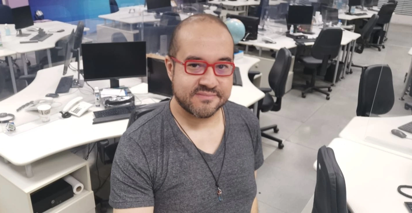 Cido Coelho homem branco calvo de barba castanha e óculos vermelhos aparece em foto em ambiente de escritório usando camisa cinza convidado do café com aner sobre inteligência artificial e jornalismo