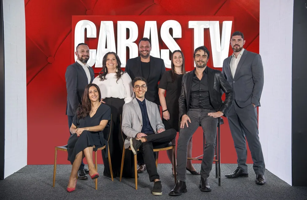 Equipe Caras Grupo Perfil posa para fotografia em cenário com fundo vermelho e as letras brancas características da Revista Caras