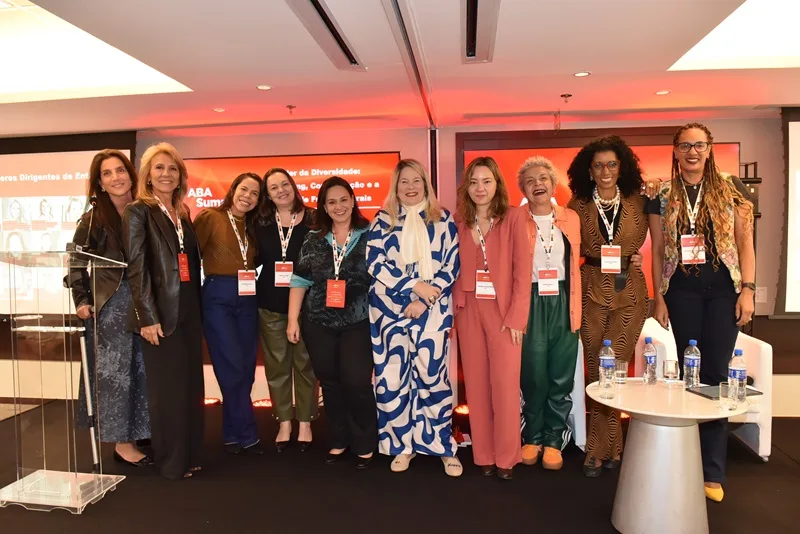 Mulheres de pé em palco diante de um fundo vermelho participantes do ABA Summit 65 Anos promovido pela ABA